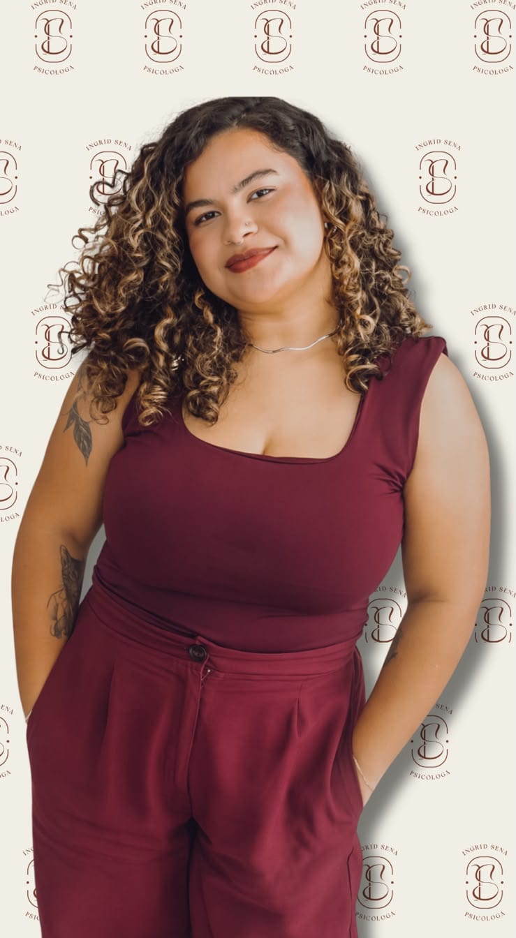 Ingrid Sena de corpo inteiro, sorrindo, diante de um painel com a marca dela